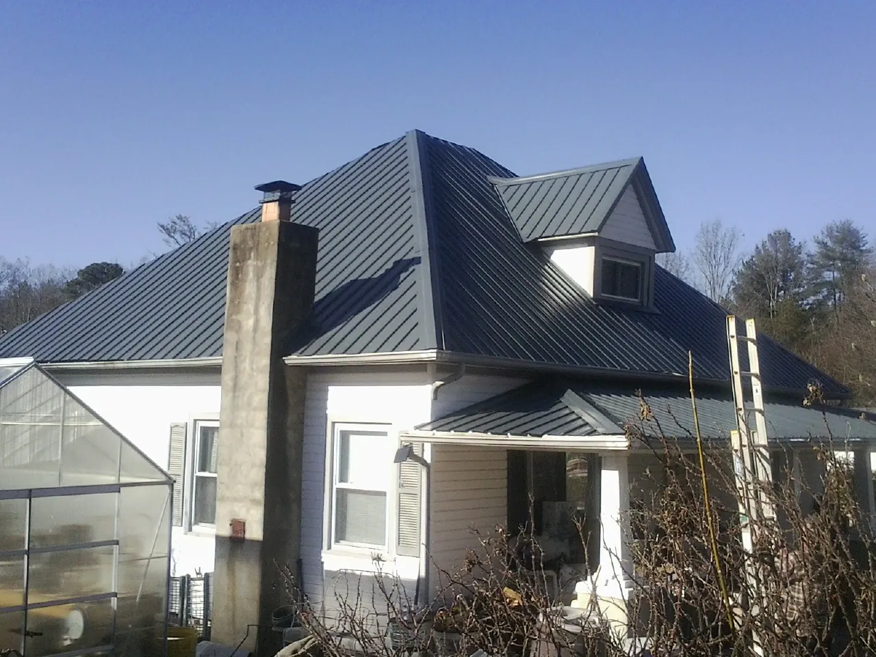 Dark blue standing seam metal roof on a white farmhouse with dormer — Slate & Tile Roof Repair by Roofing Brothers in Lolo
