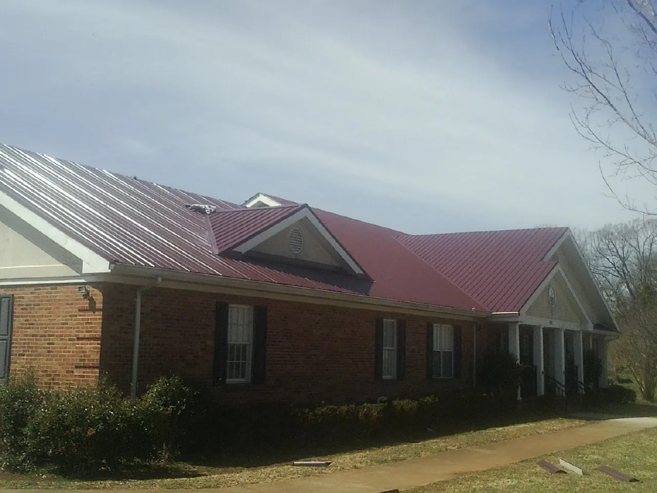 Red metal roof with gabled entries on a long brick building, from a Hail Damage Roof Repair job in Lolo