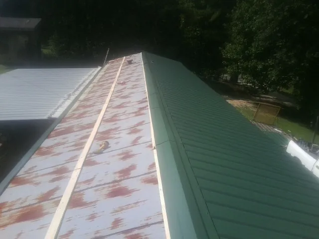 Old rusted panels beside newly installed green metal roofing — Wind Damage Roof Repair by Roofing Brothers in Lolo