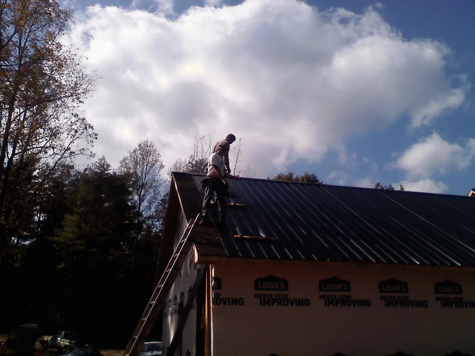 Roofer fastening dark metal panels high against a cloudy sky, from a Roof Inspection job in Lolo