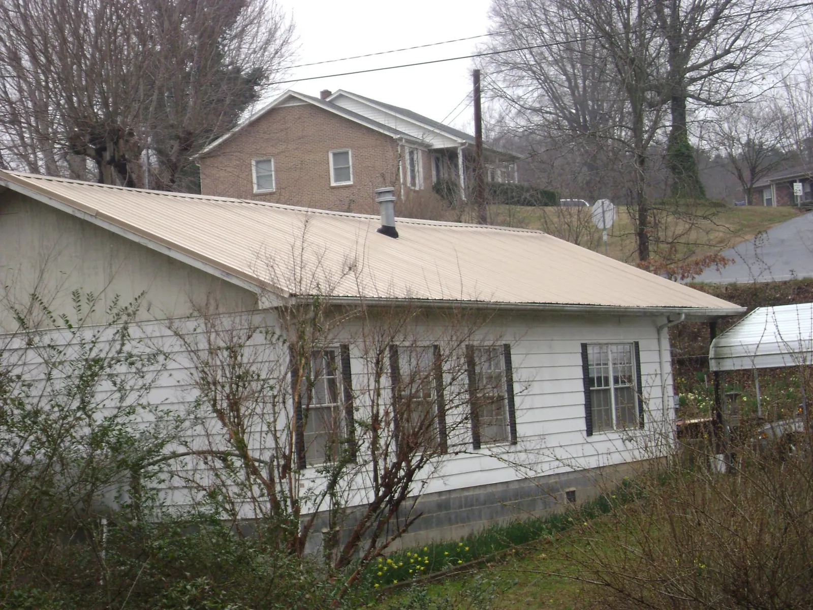 Tan metal roof on a white sided house set into a hillside — Commercial Roofing by Roofing Brothers in Lolo